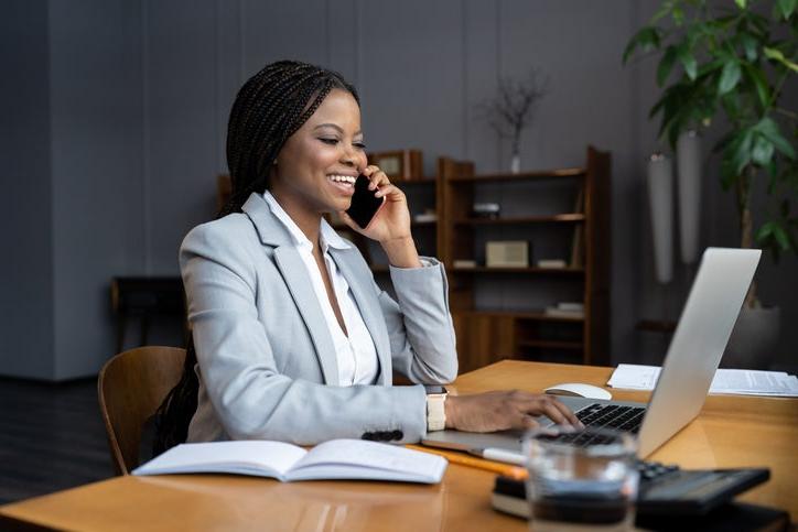 Black business woman typing on a computer and talking on phone.