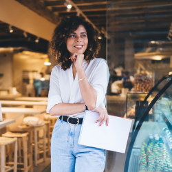 Young female entrepreneur standing outside of her cafe holding papers smiling