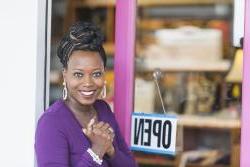Happy black business woman standing at the door of her open business.